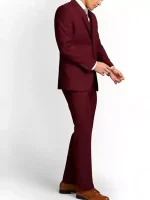 Side view of a men’s slim fit maroon 3 piece suit with matching trousers and brown dress shoes, model adjusting the sleeve cuff on a white background.