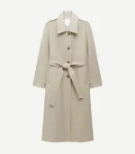 A studio product shot of the beige cotton trench coat against a plain white background. The coat is displayed with its matching fabric belt tied in a bow at the waist. It showcases the clean lines of the shirt collar, the tortoiseshell-patterned buttons, and the shoulder epaulets, presenting a classic and minimalist aesthetic.