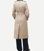 The back of the beige trench coat, showing the buckled waist belt and a central rear vent. The model is wearing black wide-leg trousers and dark sandals.