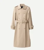 A flat studio shot of the beige double-breasted trench coat. It features contrasting light-colored buttons, shoulder epaulets, and adjustable buckled straps at the cuffs.