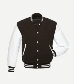 A three-quarter front view of the Brown Varsity Jacket. The angle highlights the texture of the white leather sleeves and the structured fit of the dark brown torso. It features a classic ribbed stand-up collar and matching striped detailing on the waistband and sleeve cuffs.
