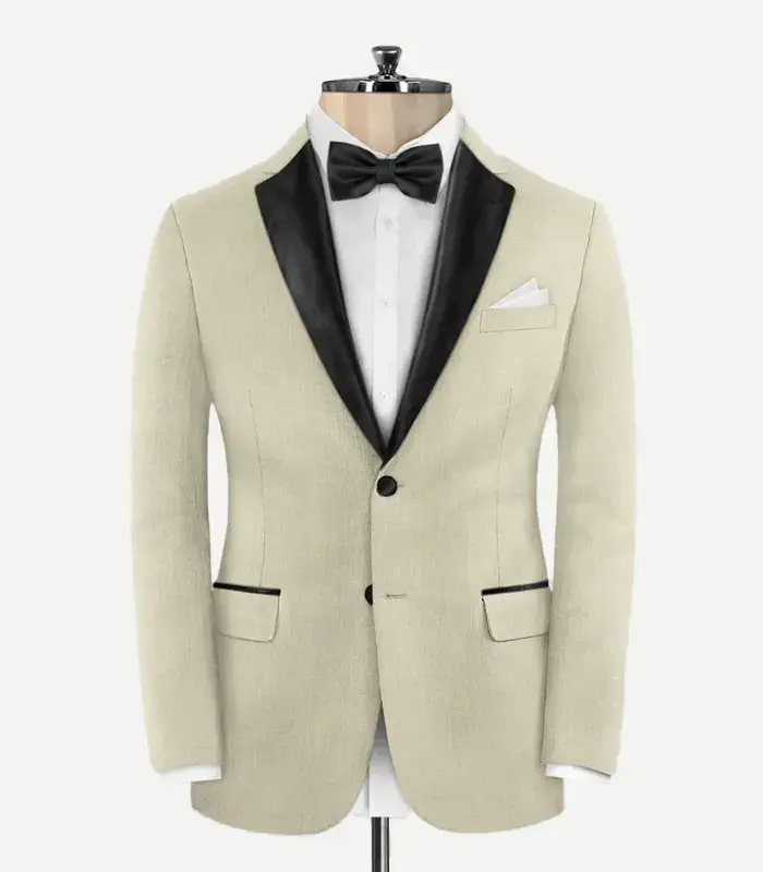 Light Beige Wool Tuxedo Jacket Front view of a slim-fit, light beige wool tuxedo jacket on a mannequin. It features contrasting black satin peak lapels, two black buttons, and jetted pockets with black satin trim. The jacket is styled with a white formal shirt and a black bow tie.