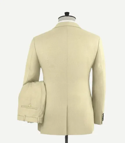 Back view of a men’s beige "Spring Latte" tuxedo jacket on a mannequin. The image shows a clean, tailored fit with a single center vent at the hem and a textured wool fabric finish. The matching trousers are shown draped over the arm of the mannequin, displaying the back pocket with a button closure and belt loops.