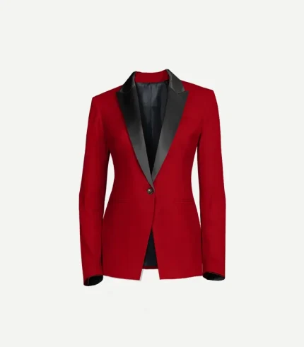 A front-facing close-up of a women’s red velvet tuxedo jacket. The design includes bold, black satin peak lapels, a single black button closure, and two horizontal jetted pockets at the waist. The interior is finished with a dark lining that is visible at the open neckline and cuffs.