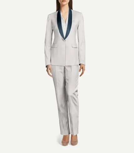 A full-length view of a woman wearing a tailored white tuxedo suit. The outfit consists of a single-button blazer with deep navy blue shawl lapels and matching slim-fit trousers with a sharp center crease. She is wearing a white button-down shirt underneath and neutral-toned pointed-toe heels.