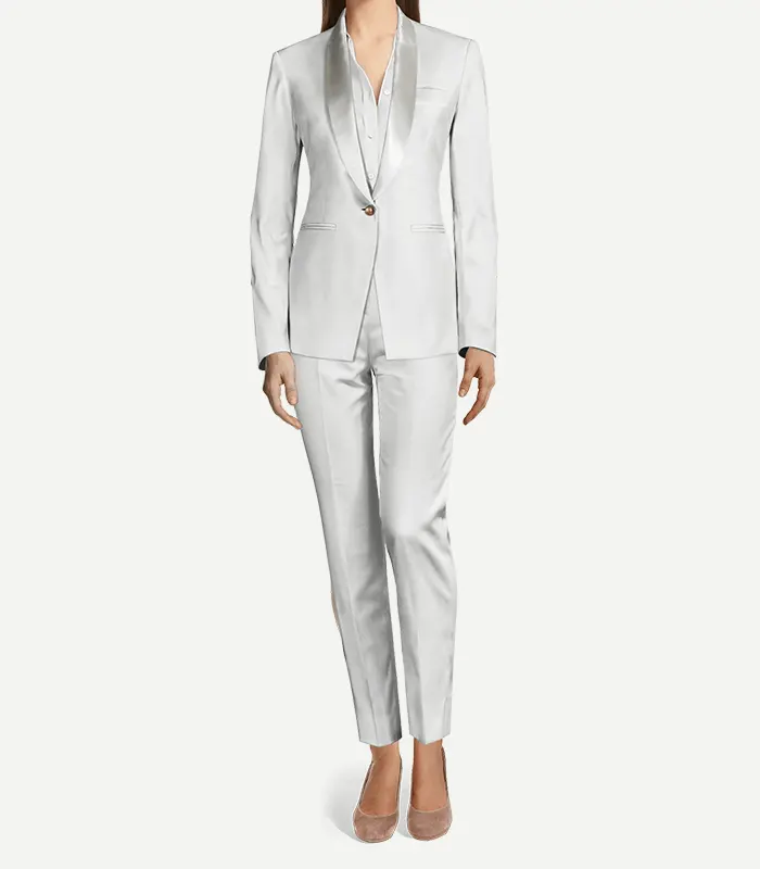 Womens White Velvet Tuxedo A woman modeling a tailored, monochromatic white velvet tuxedo. The outfit features a slim-fit blazer with a satin shawl lapel, a single gold button closure, and matching slim-leg trousers with a sharp front crease. She is wearing a white button-down shirt underneath and neutral-toned pointed-toe flats.