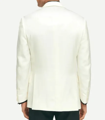 A rear view of a man wearing a structured, off-white dinner jacket. The jacket features a clean back with dual side vents and four buttons on each sleeve cuff. He is wearing black trousers that contrast with the light-colored jacket.