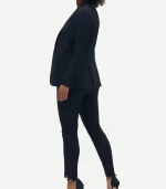 Profile view of a woman wearing a navy blue tuxedo with a single-vent blazer and slim-fit trousers, styled with dark pointed-toe heels.