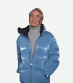 Three-quarter view of Andy Cohen wearing a glossy blue puffer jacket with a prominent high collar and visible zipper detail.