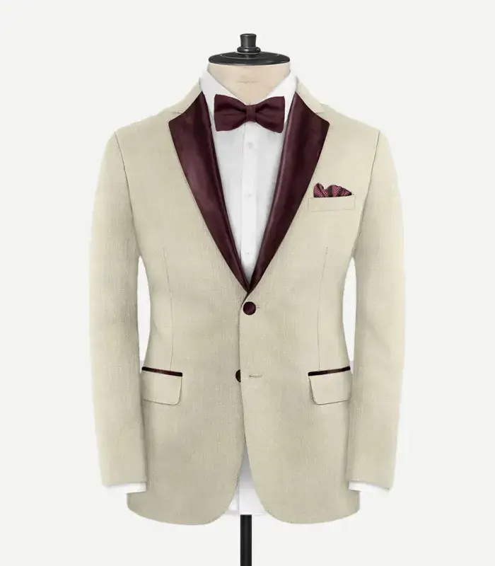 stretch-beige-wool-tuxedo-jacket-front-burgundy-lapel Front view of the Stretch Beige Wool Tuxedo Jacket featuring burgundy satin peak lapels, a single-button closure, and matching burgundy trim on the pocket flaps.