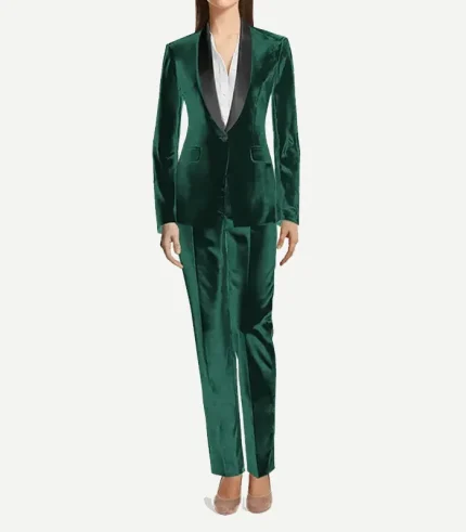 A full-length view of a woman wearing a tailored emerald green velvet tuxedo. She is styled with a crisp white button-down shirt underneath and neutral-toned pointed-toe heels. The suit features a black satin shawl lapel and straight-leg matching velvet trousers.