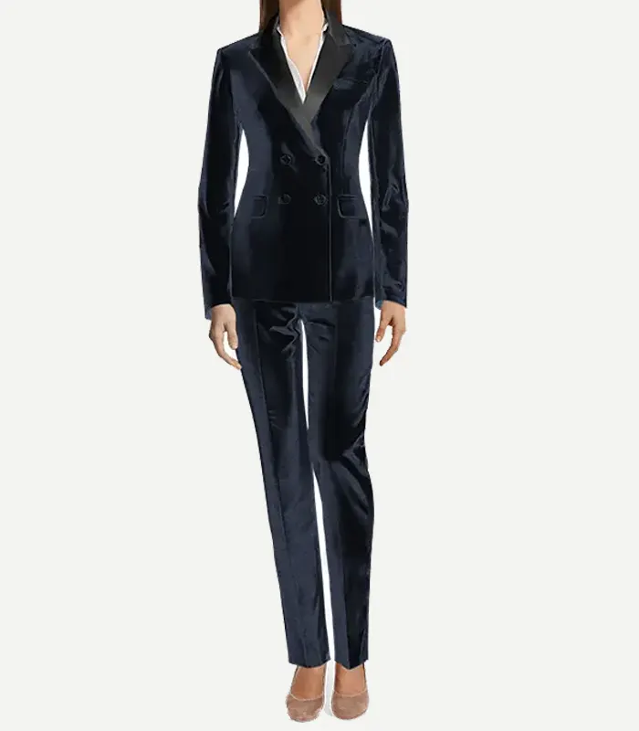 womens-navy-blue-double-breasted-velvet-tuxedo A full-length studio shot of a model wearing a tailored navy blue velvet double-breasted tuxedo. The suit is styled with a white V-neck shirt and neutral pointed-toe heels. The ensemble includes a structured jacket with satin accents and slim-fit matching trousers.