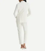 A rear view of a woman wearing an elegant, all-white tuxedo. The blazer features a clean, structured fit with a center vent, paired with slim-cut trousers and beige pointed-toe heels.