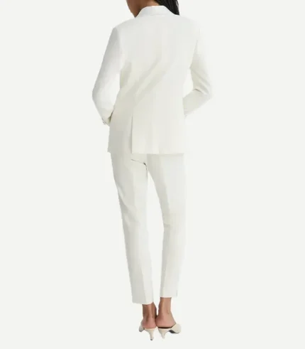 A rear view of a woman wearing an elegant, all-white tuxedo. The blazer features a clean, structured fit with a center vent, paired with slim-cut trousers and beige pointed-toe heels.