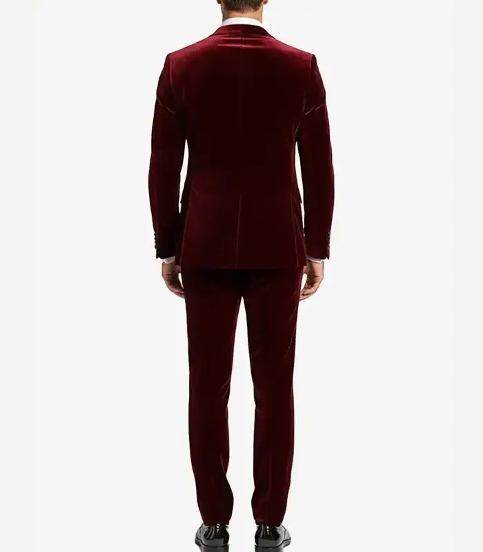 Rear view of a man wearing a structured two-piece maroon velvet tuxedo jacket and matching velvet trousers.