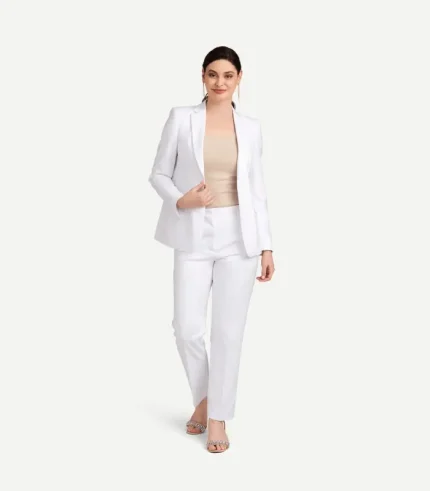 A front view product shot of a female model wearing a structured women's pearl white stretch suit jacket and matching trousers, styled over a bare chest with a minimalist gold necklace.